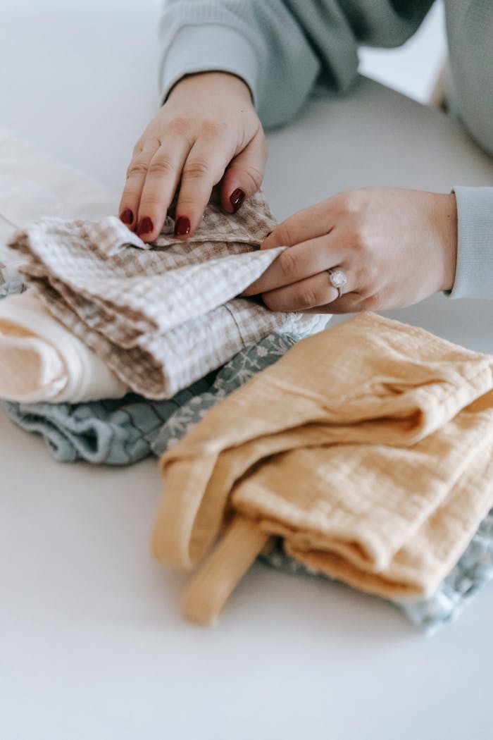 Hands folding various textiles, showcasing neat organization and home lifestyle indoors.