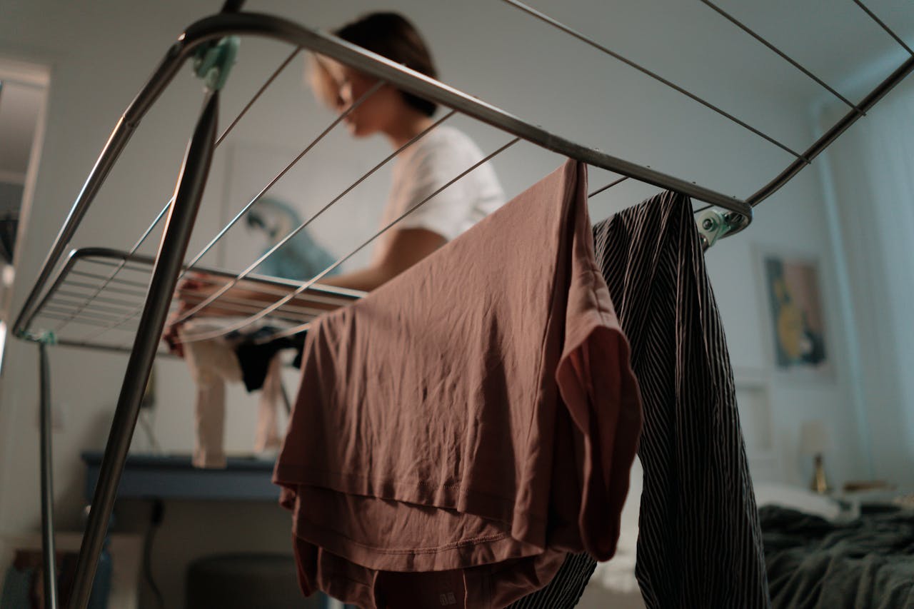 A person hanging freshly washed clothes on a drying rack at home, highlighting daily chores.
